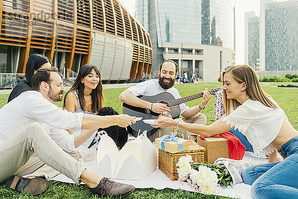 Happy man playing guitar with friends enjoying picnic in park