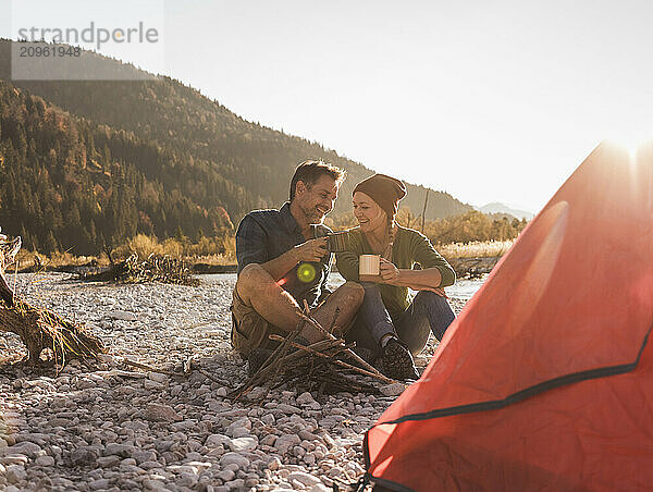 Cheerful couple enjoying coffee sitting at riverside