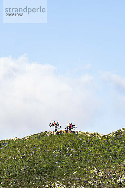 Friends standing with bicycles on mountain under cloudy sky