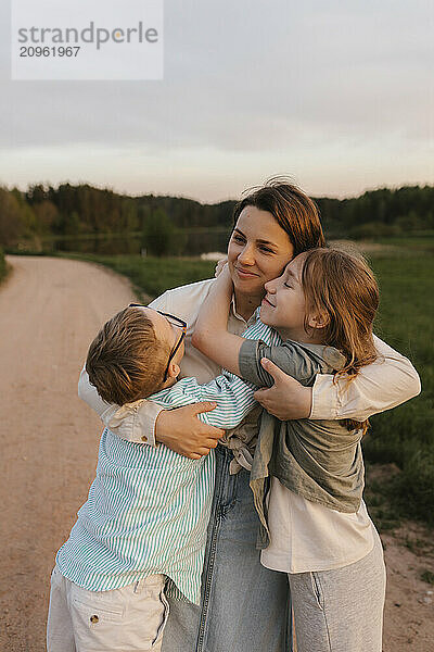 Children embracing mother standing near meadow