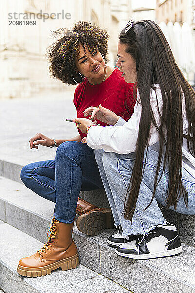 Young woman gesturing and sitting beside tourist friend on steps