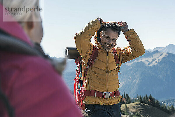 Smiling man wearing hood of jacket standing on mountain