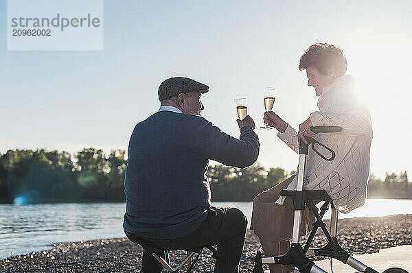 Happy senior couple toasting champagne near river on sunny day