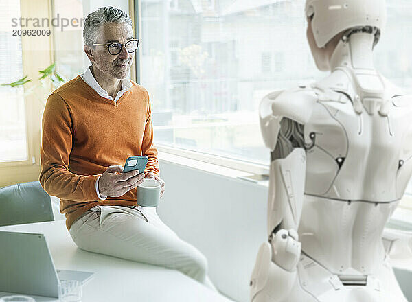 Businessman sitting and looking at cyborg in office