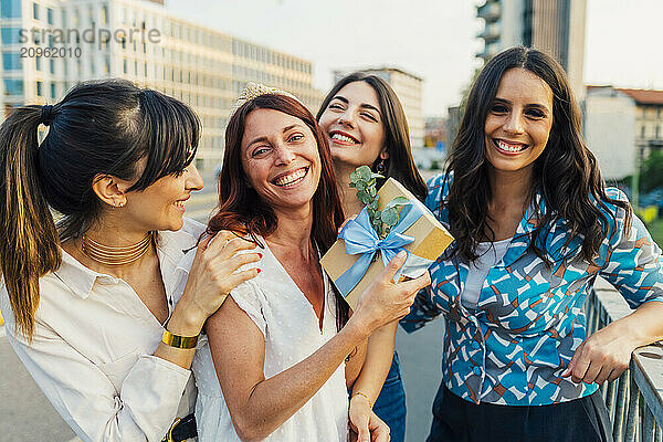 Cheerful woman holding gift box with friends in front of buildings