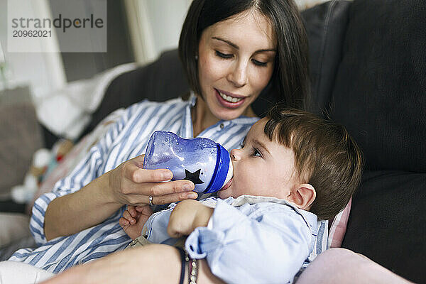 Mother feeding baby boy with milk bottle at home