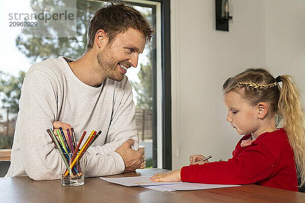 Smiling father with daughter drawing on paper at home