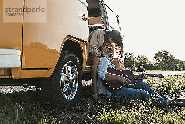 Romantic woman embracing man playing guitar sitting near van