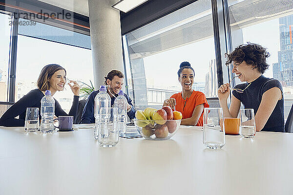 Happy multiracial business colleagues sitting at table in meeting room at office