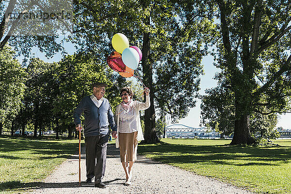 Happy couple walking together with balloons in park on sunny day