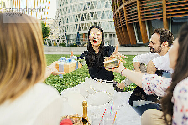 Friends giving gifts to woman sitting on blanket in park