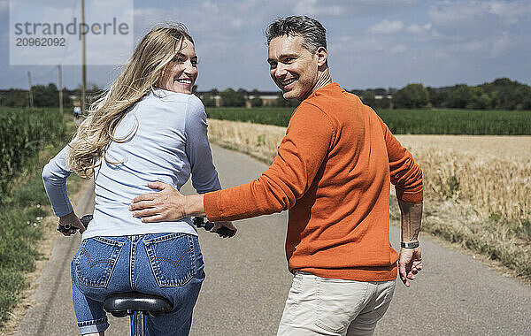 Cheerful woman riding bicycle and enjoying with man on road