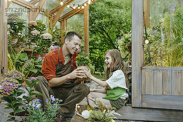 Man with daughter looking at potted plant and sitting at plant nursery