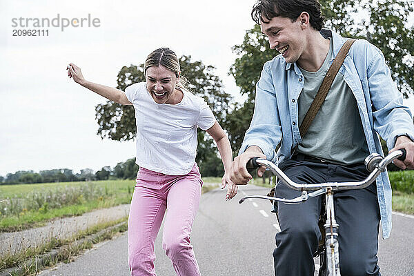 Carefree young woman with boyfriend riding bicycle on road