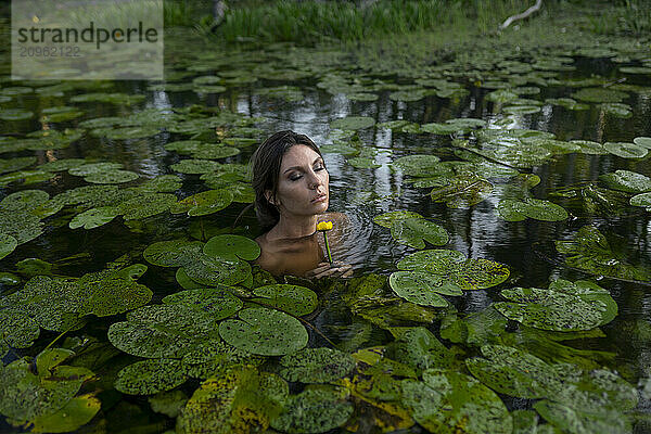 Woman with eyes closed surrounded by lily pads in pond