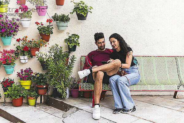 Smiling couple using smart phone and sitting on bench