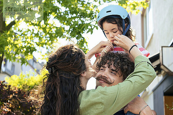 Man looking at woman adjusting daughter's helmet