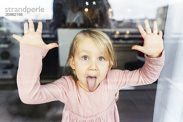 Mischief girl sticking out tongue and looking through window