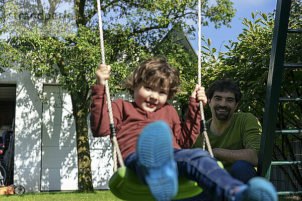 Father spending leisure time with son swinging in back yard