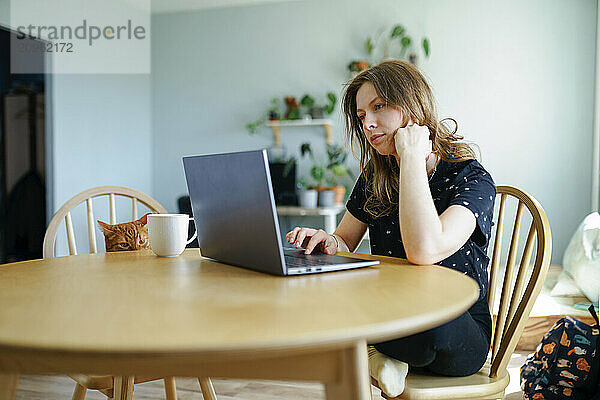 Freelancer working on laptop at table in home