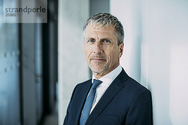 Confident businessman in suit near wall at office