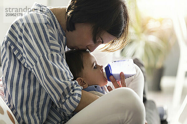 Mother kissing and feeding son with milk at home