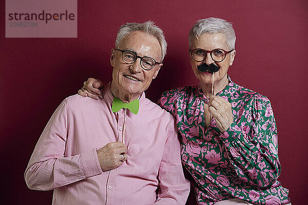 Happy senior couple posing with fake moustache and bowtie