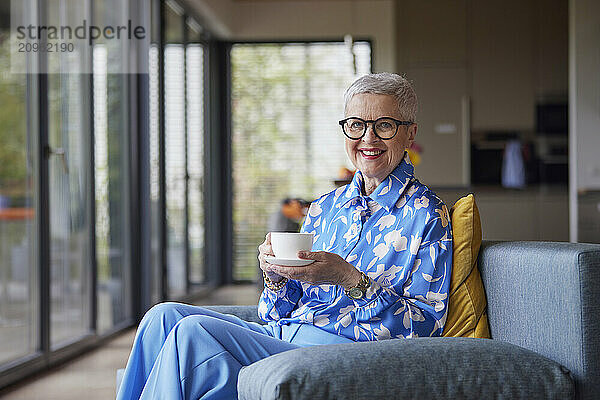 Smiling senior woman sitting on couch at home with cup of coffee