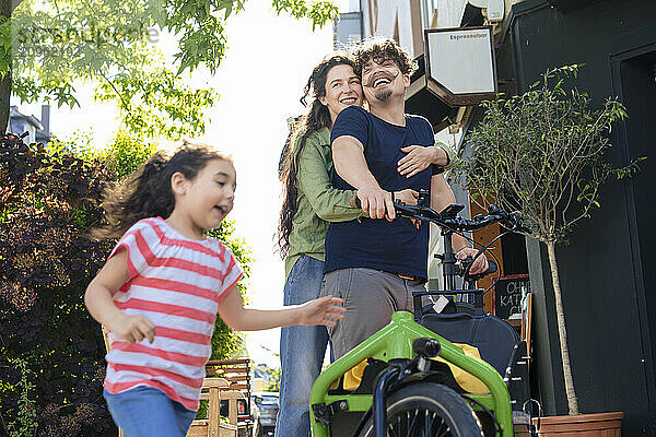 Woman embracing man and standing near cargo bike with daughter at street