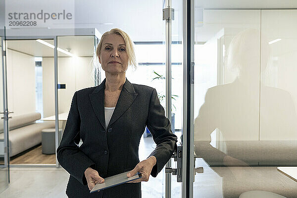 Businesswoman holding tablet PC and leaning on door at office