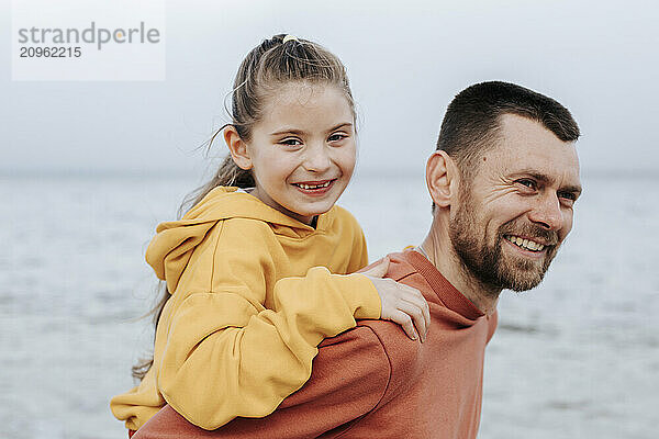 Happy father giving piggy back ride to daughter at beach