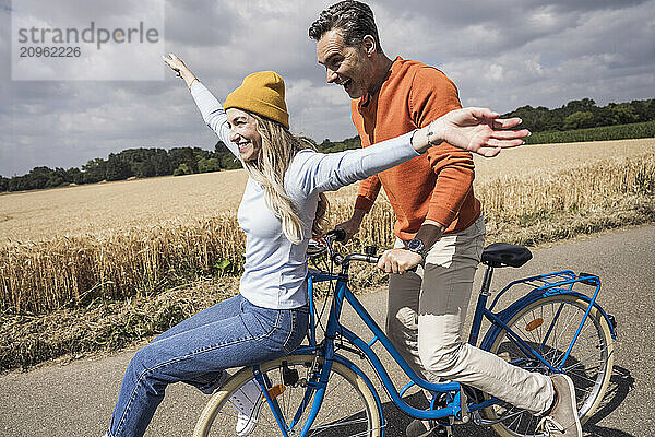 Happy man and woman enjoying bicycle ride in front of field