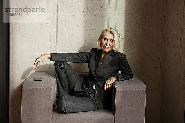 Senior businesswoman sitting on armchair near wall at office