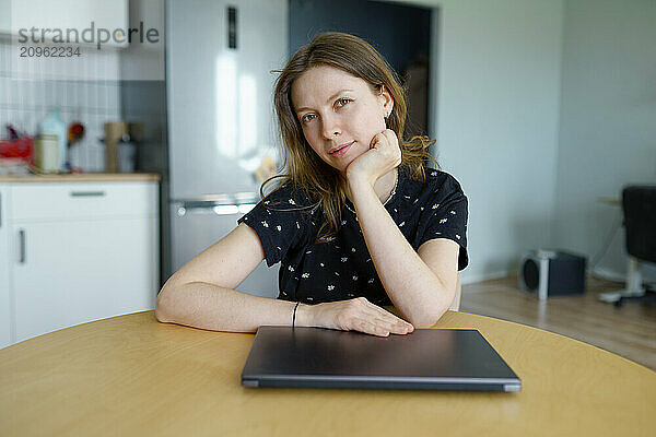 Freelancer sitting with laptop and hand on chin at table