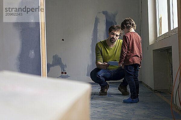 Father crouching and talking with son standing in new apartment