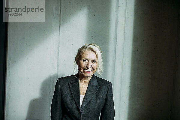 Happy senior businesswoman near wall at office