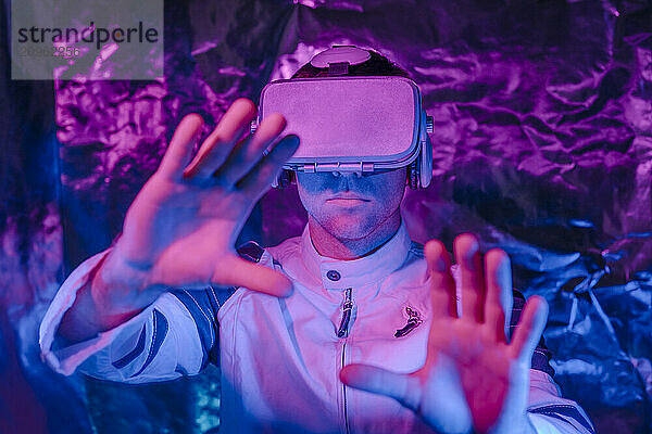 Man wearing virtual reality simulator and gesturing in neon lights