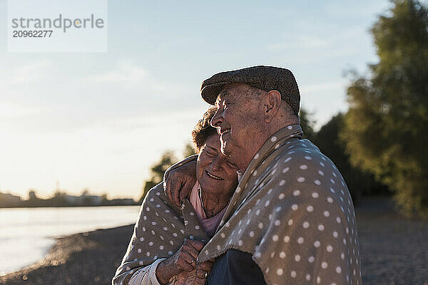 Senior couple wrapped in blanket at sunset