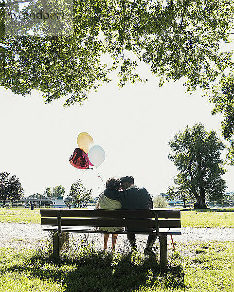 Romantic senior couple sitting with balloons on park bench