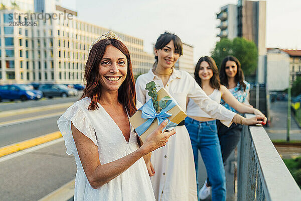 Happy woman holding gift box with friends in background