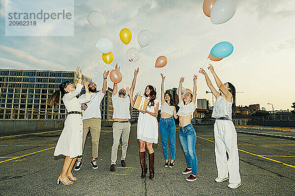 Cheerful friends celebrating woman's birthday with balloons on road