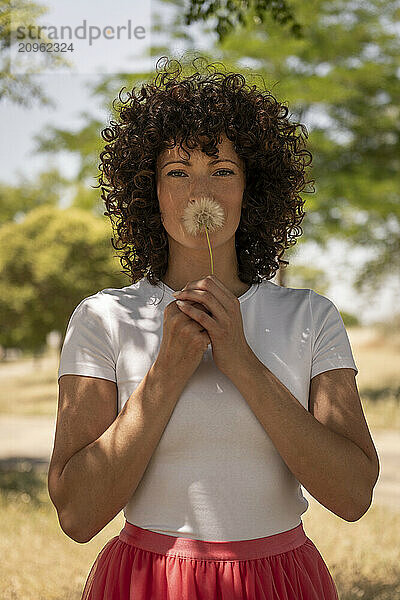 Woman with curly hair holding dandelion at park