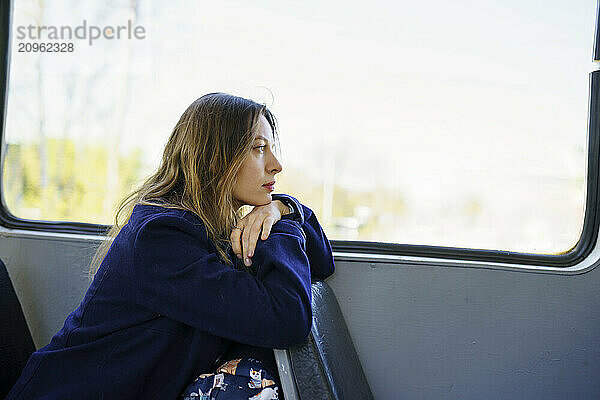 Contemplative woman leaning on seat and looking through window