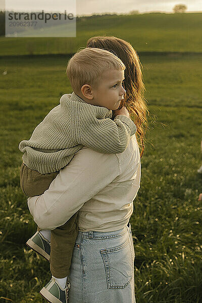 Mother carrying son in arms at meadow