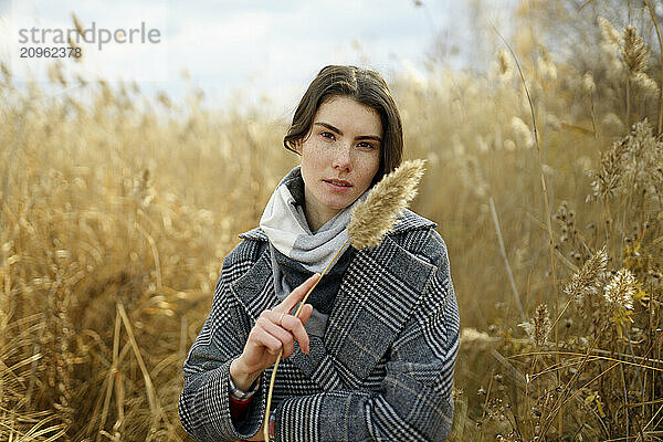 Woman in trench coat holding pampas in field