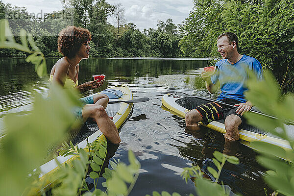 Happy friends eating watermelon on paddleboard in lake