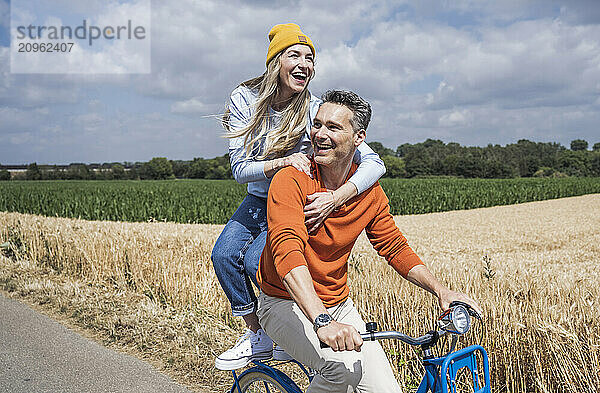 Cheerful loving couple enjoying bicycle ride in front of field on sunny day