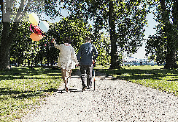 Senior couple walking with balloons in park