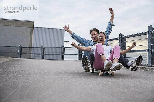 Cheerful young couple riding on skateboard at bridge