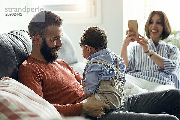 Woman photographing father and son spending leisure time at home